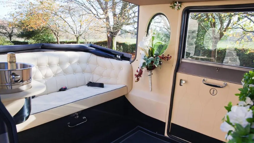 Interior view of a silver Imperial wedding car with cream leather seating, polished wood trim, and floral decoration on the side door.