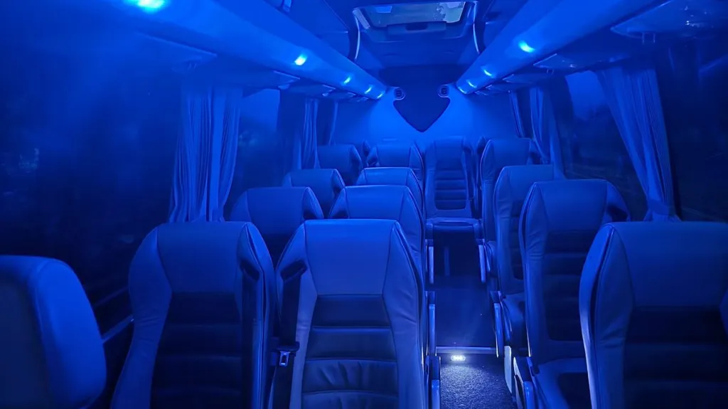 Inside view of a Mercedes minibus interior illuminated with blue LED mood lighting along the ceiling and aisles.