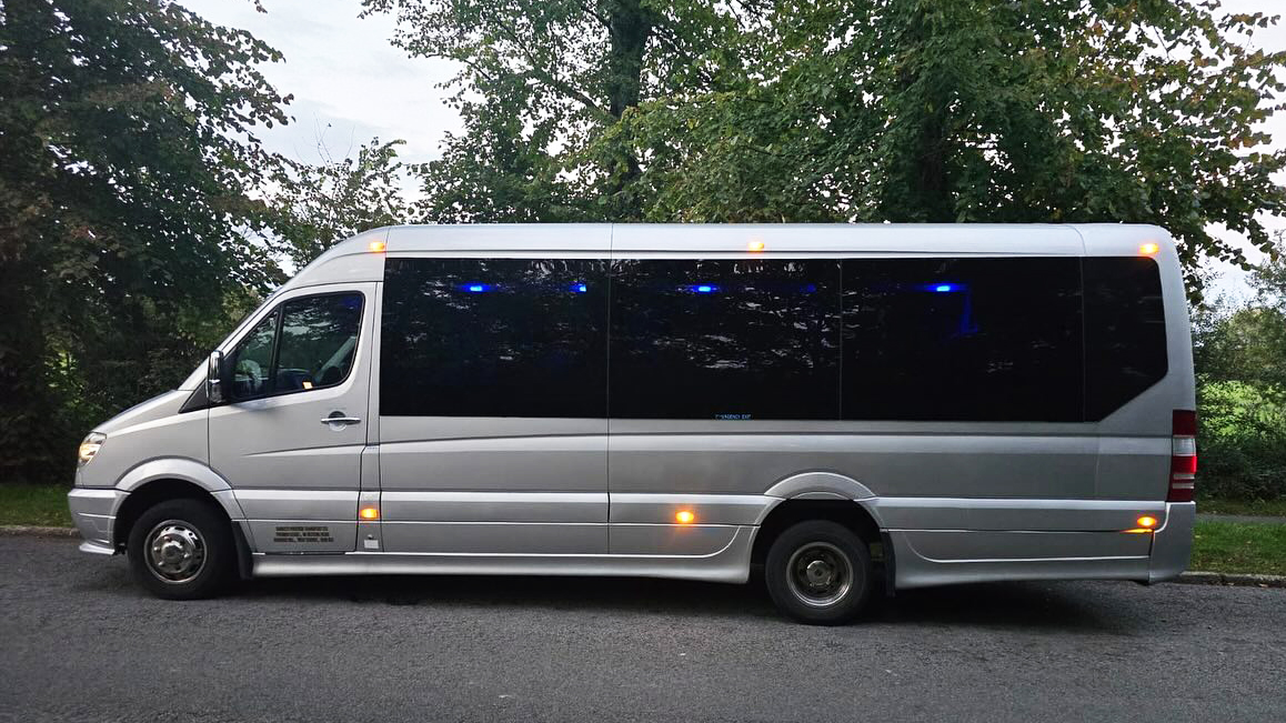 Side view of a silver Mercedes 16-seater minibus showing large panoramic windows and sleek modern styling.