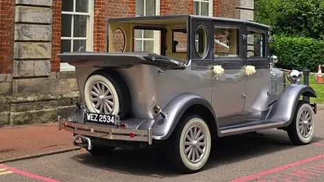 Rear view of a silver Imperial vintage wedding car with the convertible soft-top roof open, showing the spare wheel and chrome bumper.