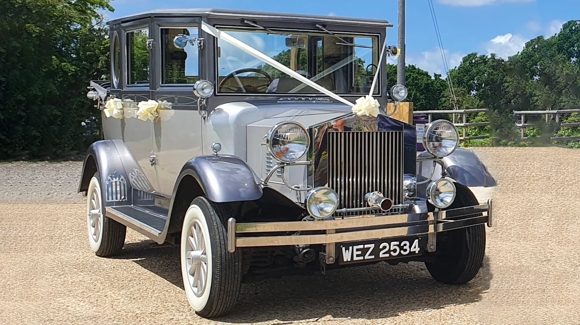 Silver Imperial convertible vintage-style wedding car parked on a sunny lane in Sussex, with the roof down and decorated for a wedding.
