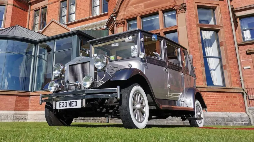 Silver Imperial convertible wedding car decorated with white ribbons parked in front of a red-brick venue in Antrim.