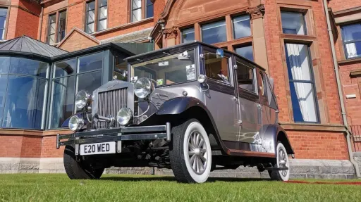 Silver Imperial convertible wedding car decorated with white ribbons parked in front of a red-brick venue in Antrim.