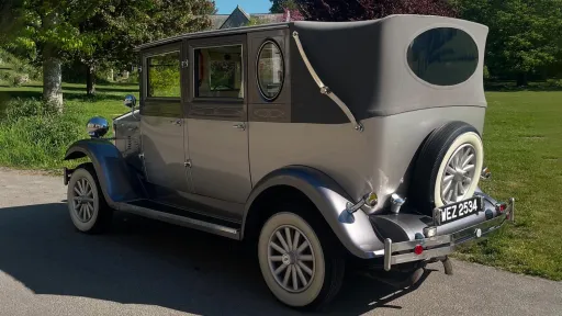 Side view of a silver Imperial vintage wedding car with its soft-top roof closed, parked in open countryside in Sussex.