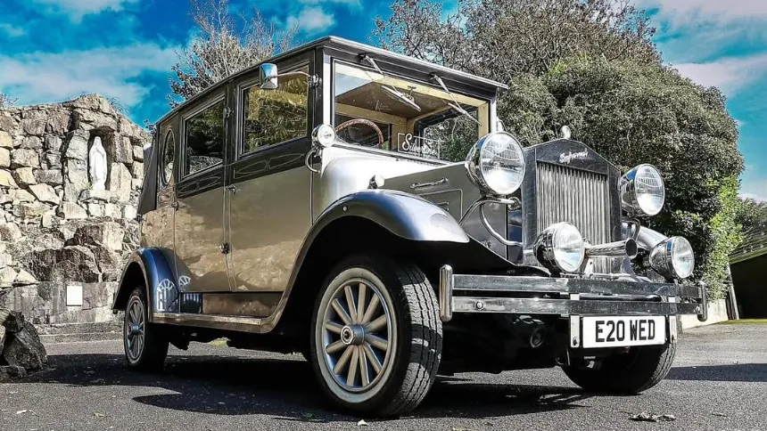 Two-tone silver Imperial vintage wedding car with chrome headlights and sweeping wings parked under a bright blue sky in Antrim.