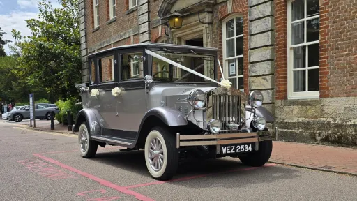 Silver Imperial vintage wedding car parked on a quiet Sussex street, gleaming in the sunlight with chrome details and ribbons