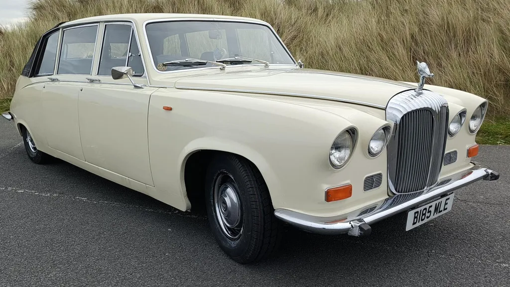 Front right view of a Daimler DS420 limousine with classic round headlamps and chrome bumper parked on the coast.