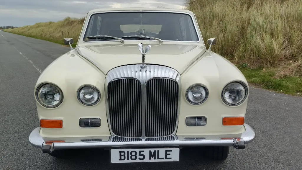 Full front view of an ivory Daimler DS420 limousine with a polished chrome grille and twin headlight design.