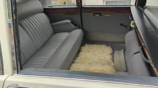 Close-up view of the rear grey leather seating inside a classic Daimler limousine featuring fold-out occasional seats and soft floor rugs.