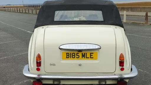 Rear view of an ivory Daimler limousine showing its distinctive black semi-convertible roof and chrome detailing.