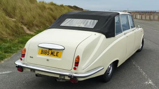 Ivory Daimler limousine viewed from the rear right side, showcasing the semi-convertible black roof and elegant long body style.