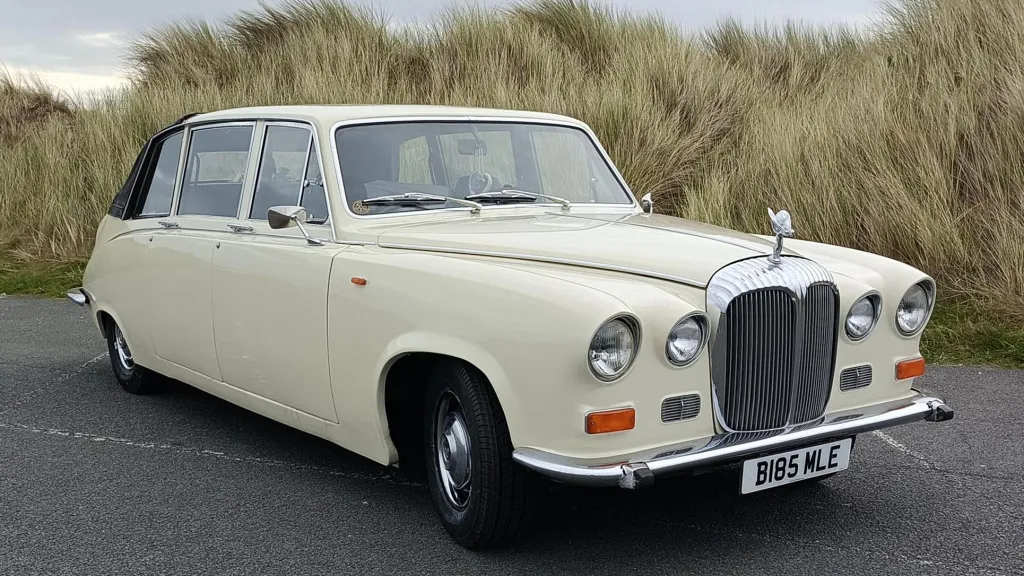 Right side view of an ivory Daimler DS420 limousine parked along the Lancashire coast with its semi-convertible roof closed.
