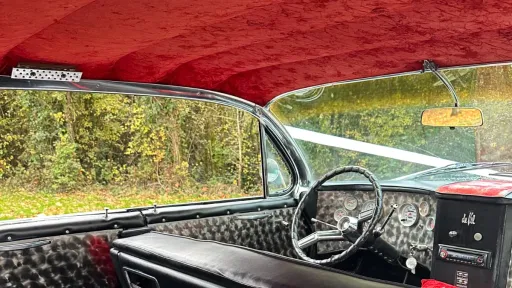 Vintage American car interior with black seating, red headliner and chrome dashboard trim.