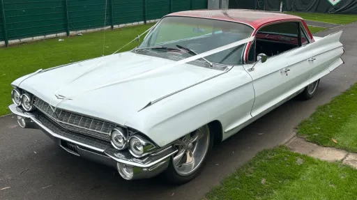 White vintage Cadillac with custom red roof decorated with wedding ribbons.