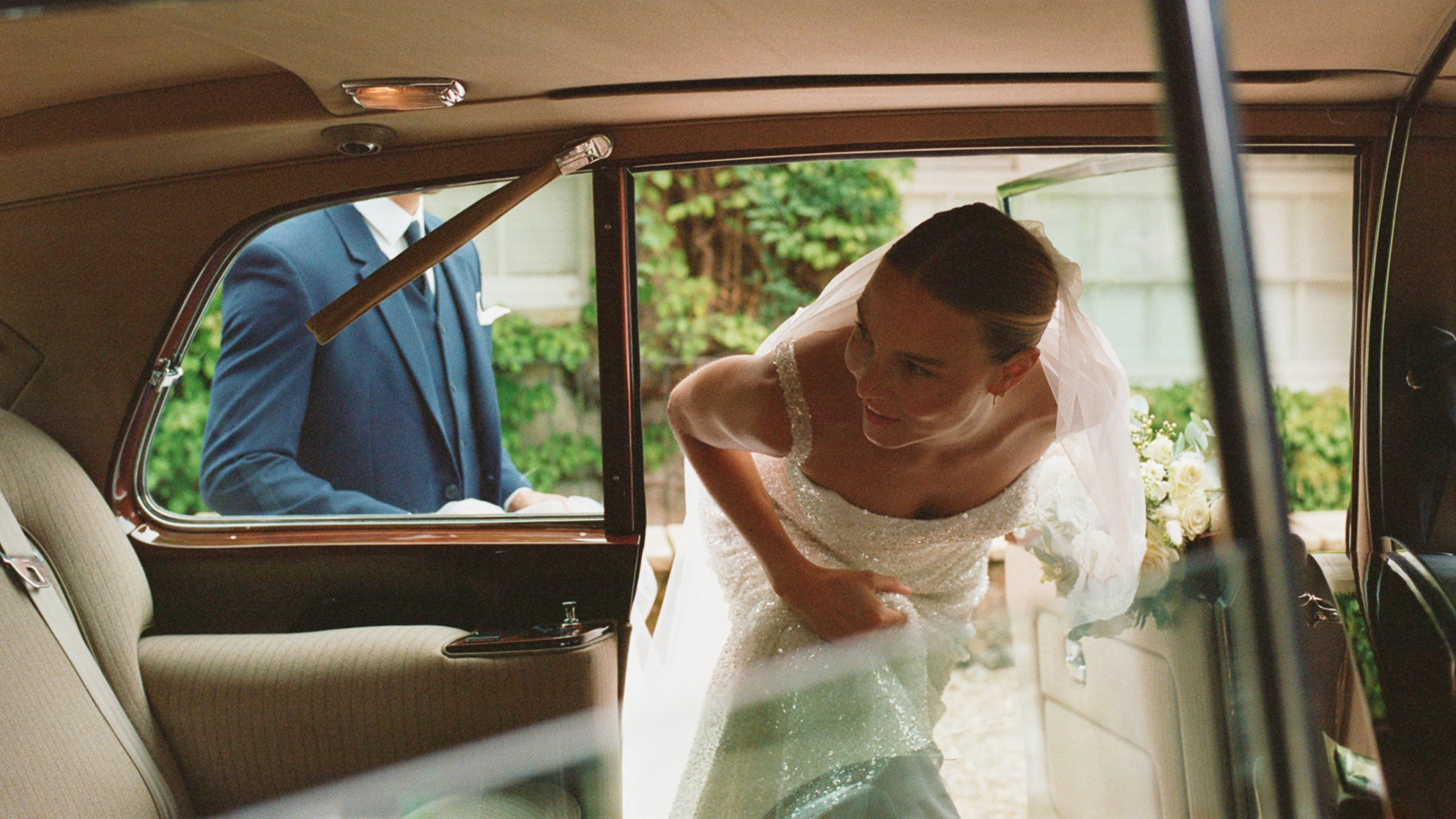 Bride leaning into the rear of a Rolls-Royce Phantom limousine in her wedding dress.