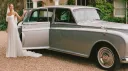 Bride standing beside a classic Rolls-Royce Phantom limousine with her white gown flowing.