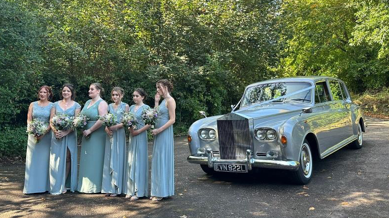 Alt text: Bridesmaids posing next to a silver Rolls-Royce Mk6 Phantom at a country estate.