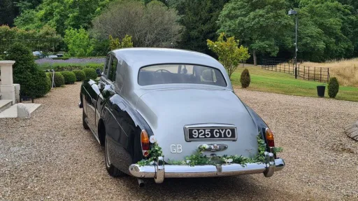 rear three-quarter angle of classic green Rolls-Royce with silver bonnet and floral decoration attached to the rear chrome bumper