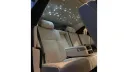 Rear interior of a Rolls-Royce Ghost showing tan leather seats and the illuminated starlight-style roof, photographed at night from the back seat.