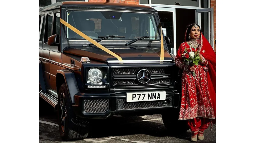 Asian bride standing beside a black Mercedes G-Wagon decorated with wedding ribbons