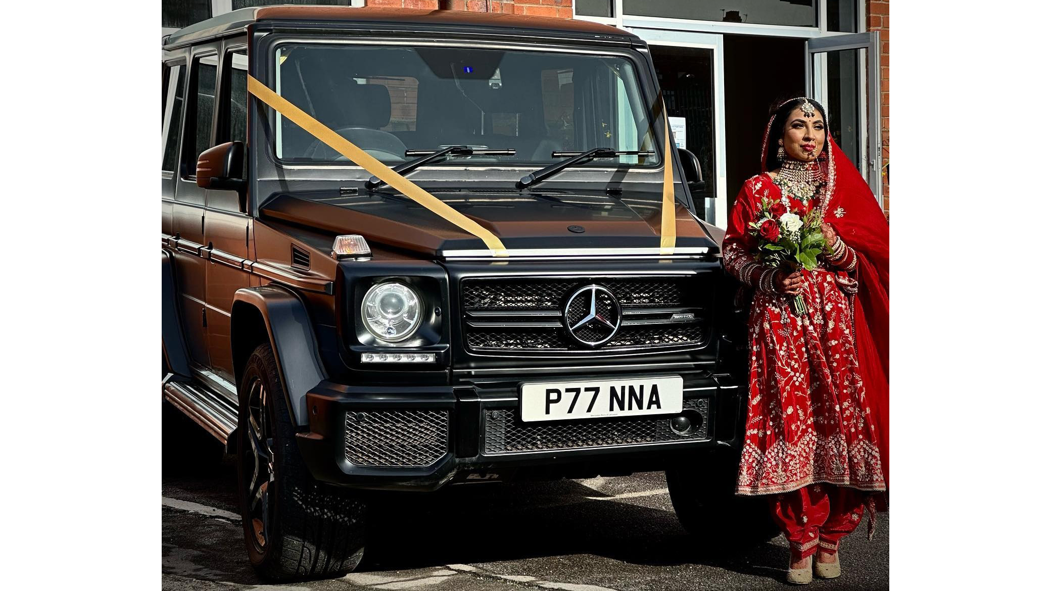 Asian bride standing beside a black Mercedes G-Wagon decorated with wedding ribbons