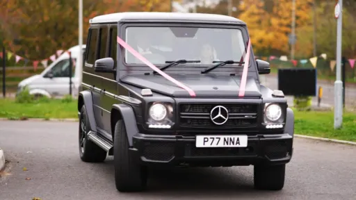 Black Mercedes G-Wagon decorated with white wedding ribbon outside a venue