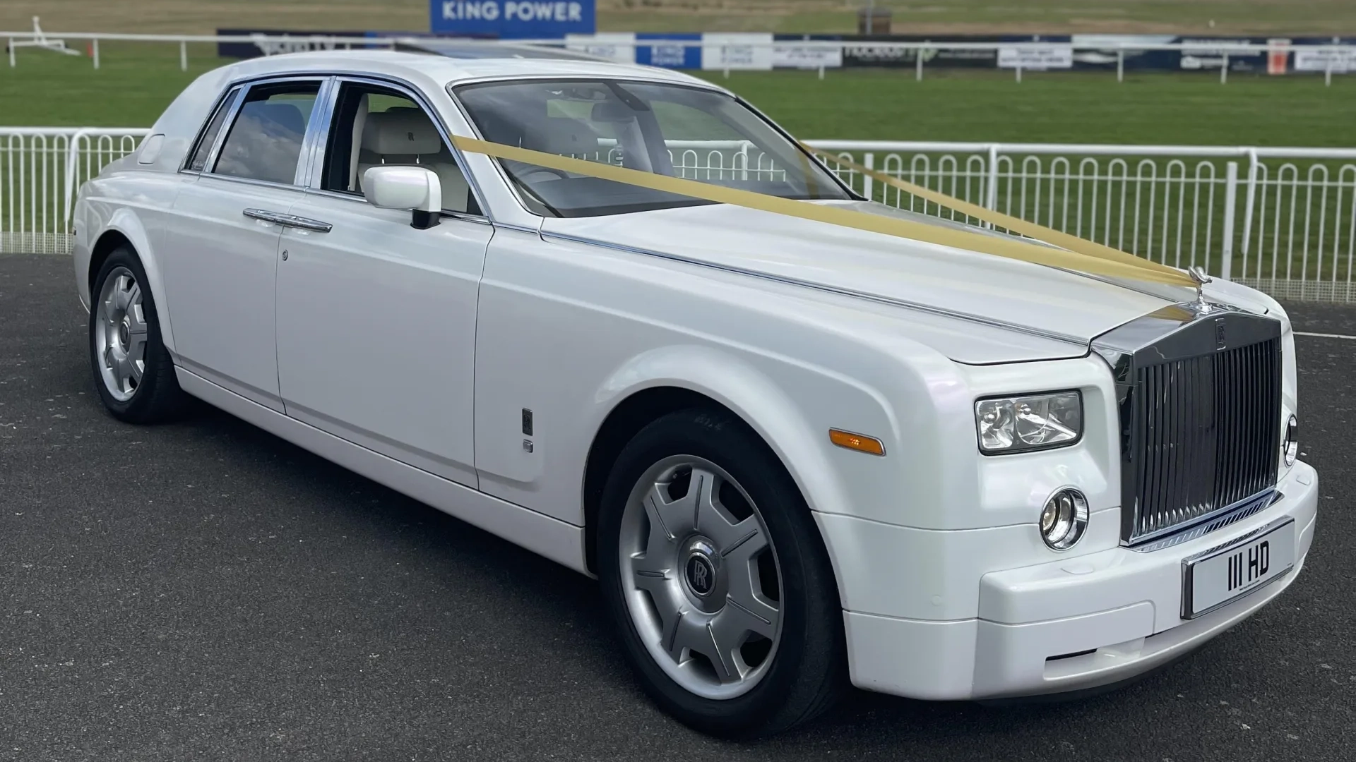 White Rolls-Royce Phantom parked outside, showcasing its long wheelbase, polished chrome grille and cream leather interior visible through the windows.