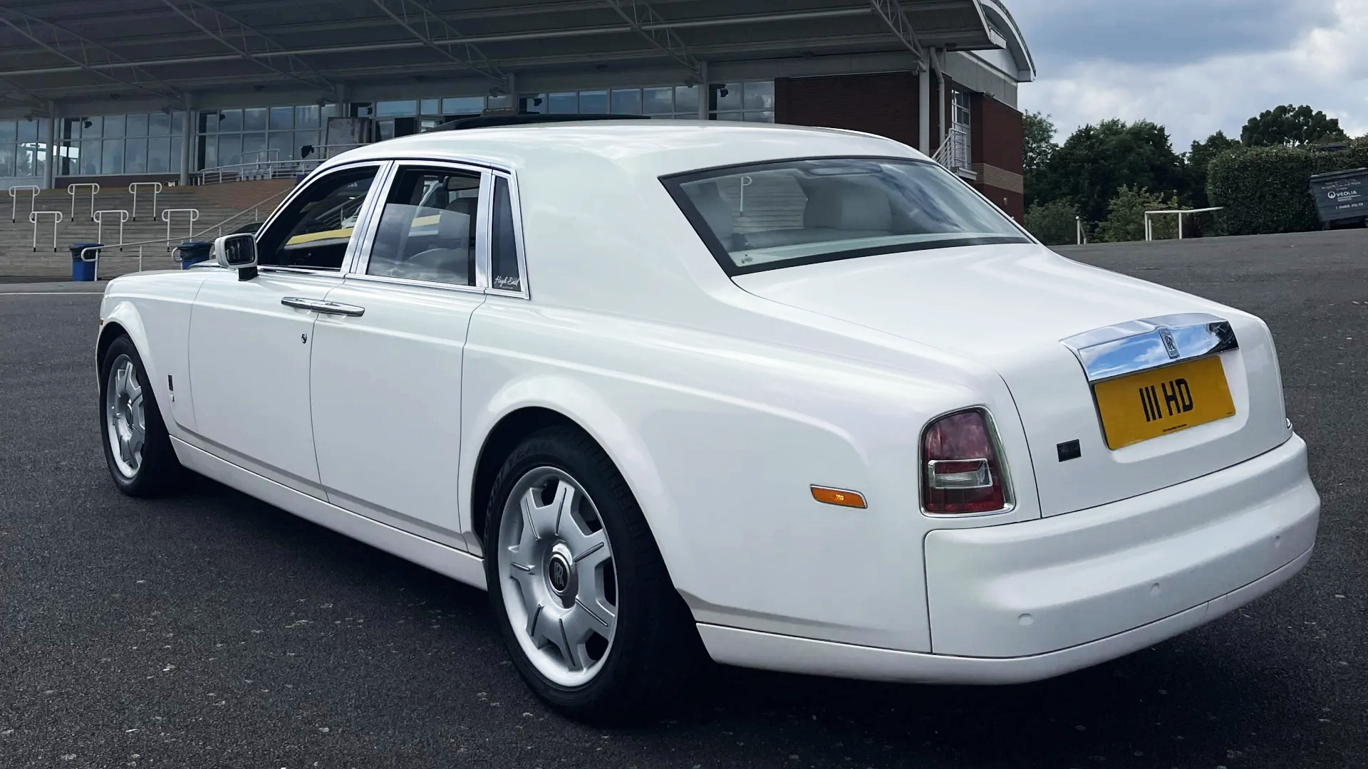 Rear view of a white Rolls-Royce Phantom parked on a quiet road, highlighting its signature tail lights and elegant silhouette.