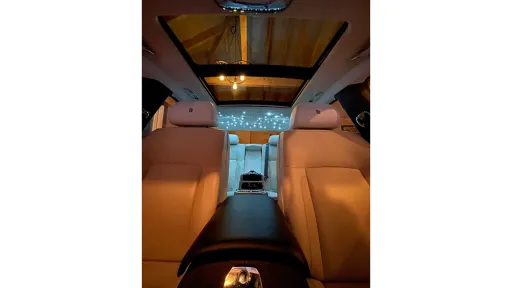 View from the front looking backward inside a Rolls-Royce Ghost, highlighting the cream leather interior and ambient lighting along the centre console.