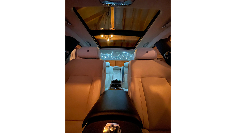View from the front looking backward inside a Rolls-Royce Ghost, highlighting the cream leather interior and ambient lighting along the centre console.