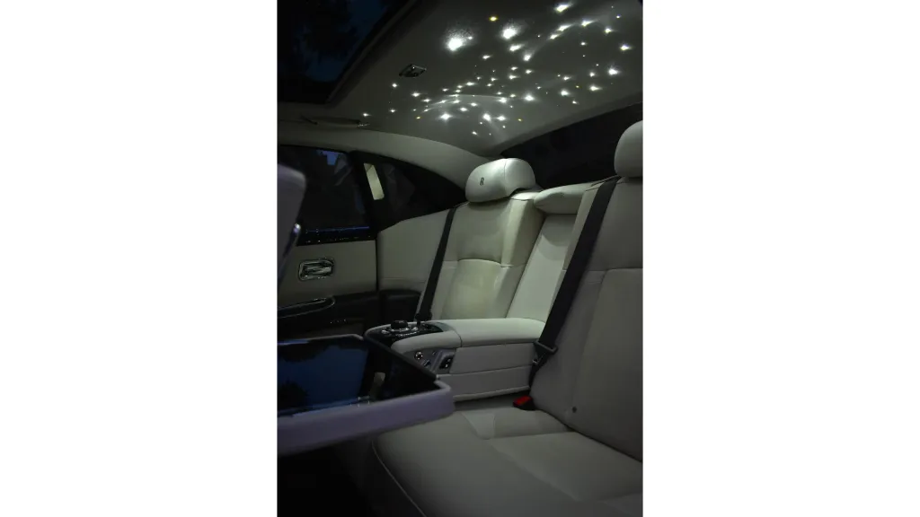 Interior photo of the Rolls-Royce Ghost’s starlight-style headliner glowing at night above the cream leather rear seats.