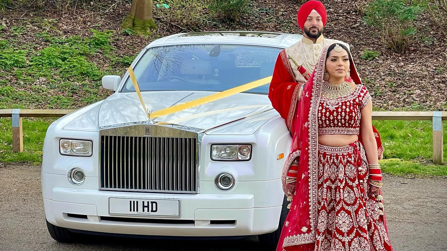 White Rolls-Royce Phantom parked near a building, with an Asian bride and groom posing beside the front grille.