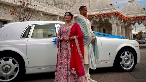 White Rolls-Royce Phantom parked outside a temple, with an Asian couple dressed in traditional attire standing beside the car.