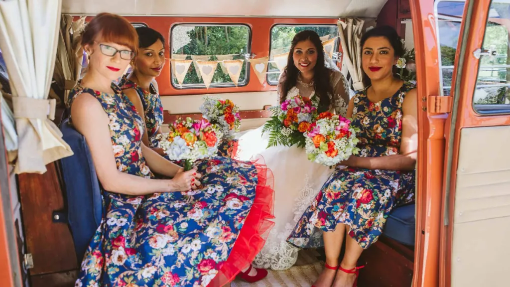 Bridesmaids sitting inside a VW campervan with colourful dresses and flowers