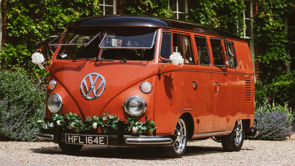 Volkswagen Splitscreen Campervan in Coral colour decorated with wedding flowers on its front bumber