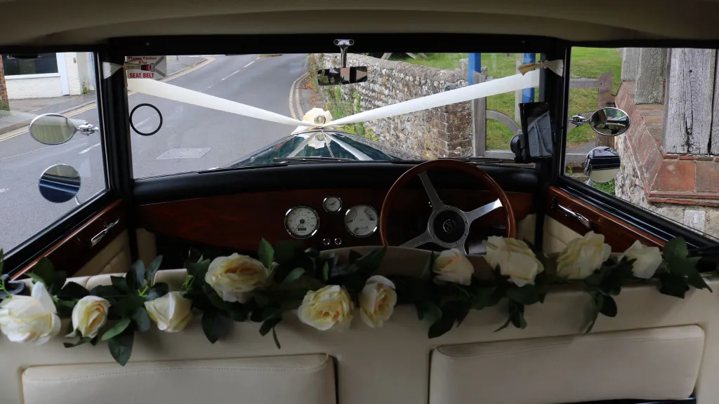 Dashboard and driver’s cabin of the Regent wedding car, featuring wood panelling, cream trim and white flower decorations across the dashboard.
