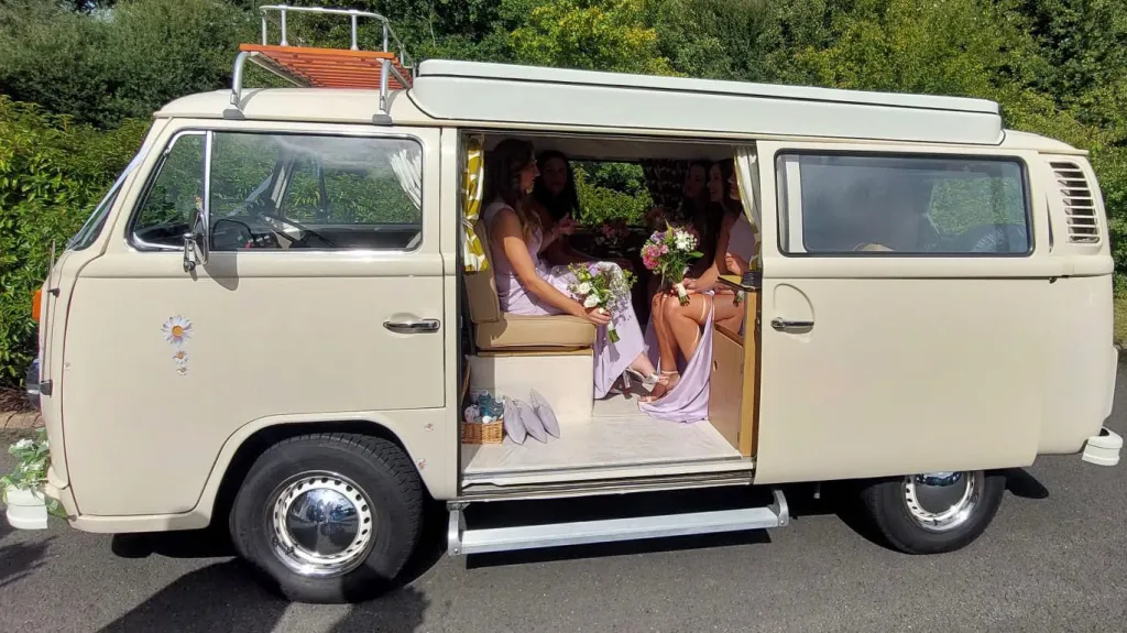 Left side view of cream Classic VW campervan with wedding guests seating inside the vehicle