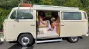 Left side view of cream Classic VW campervan with wedding guests seating inside the vehicle
