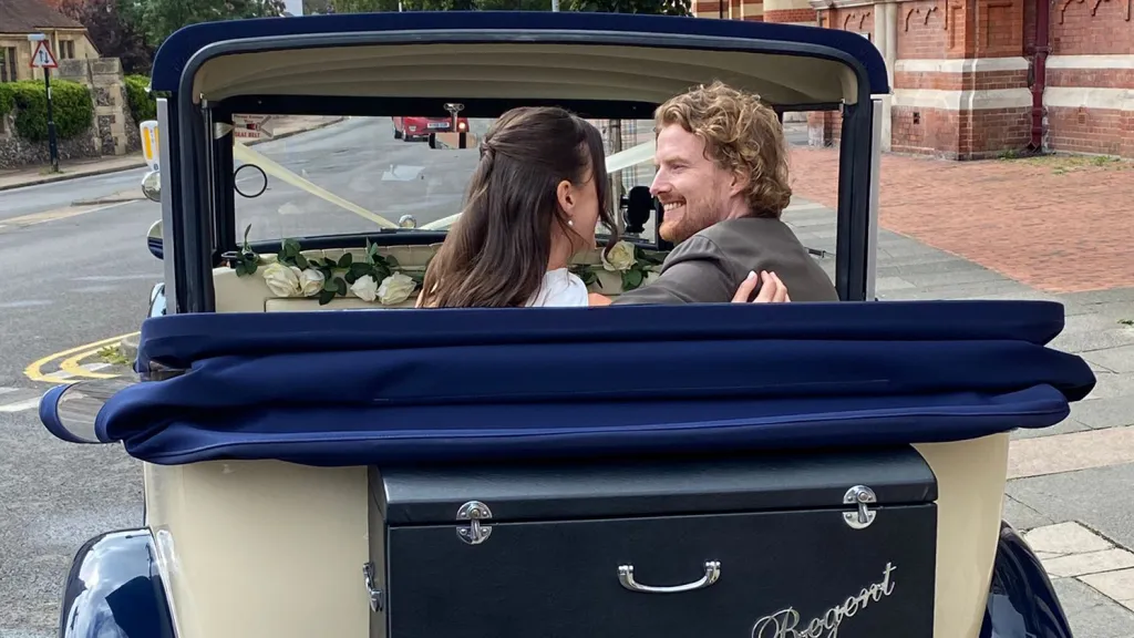Rear view of a newly-married couple smiling together in the back seat of the Regent convertible with the navy roof folded down.