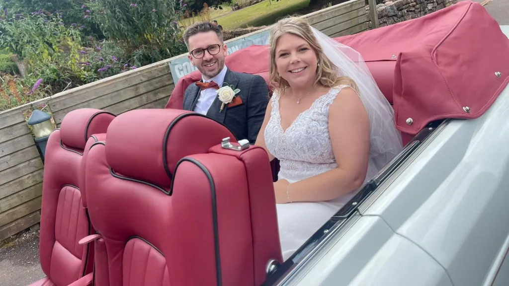 Young newly wed couple seating inside a convertible white rolls-royce corniche with Burgundy leather seats