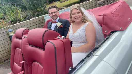 Young newly wed couple seating inside a convertible white rolls-royce corniche with Burgundy leather seats