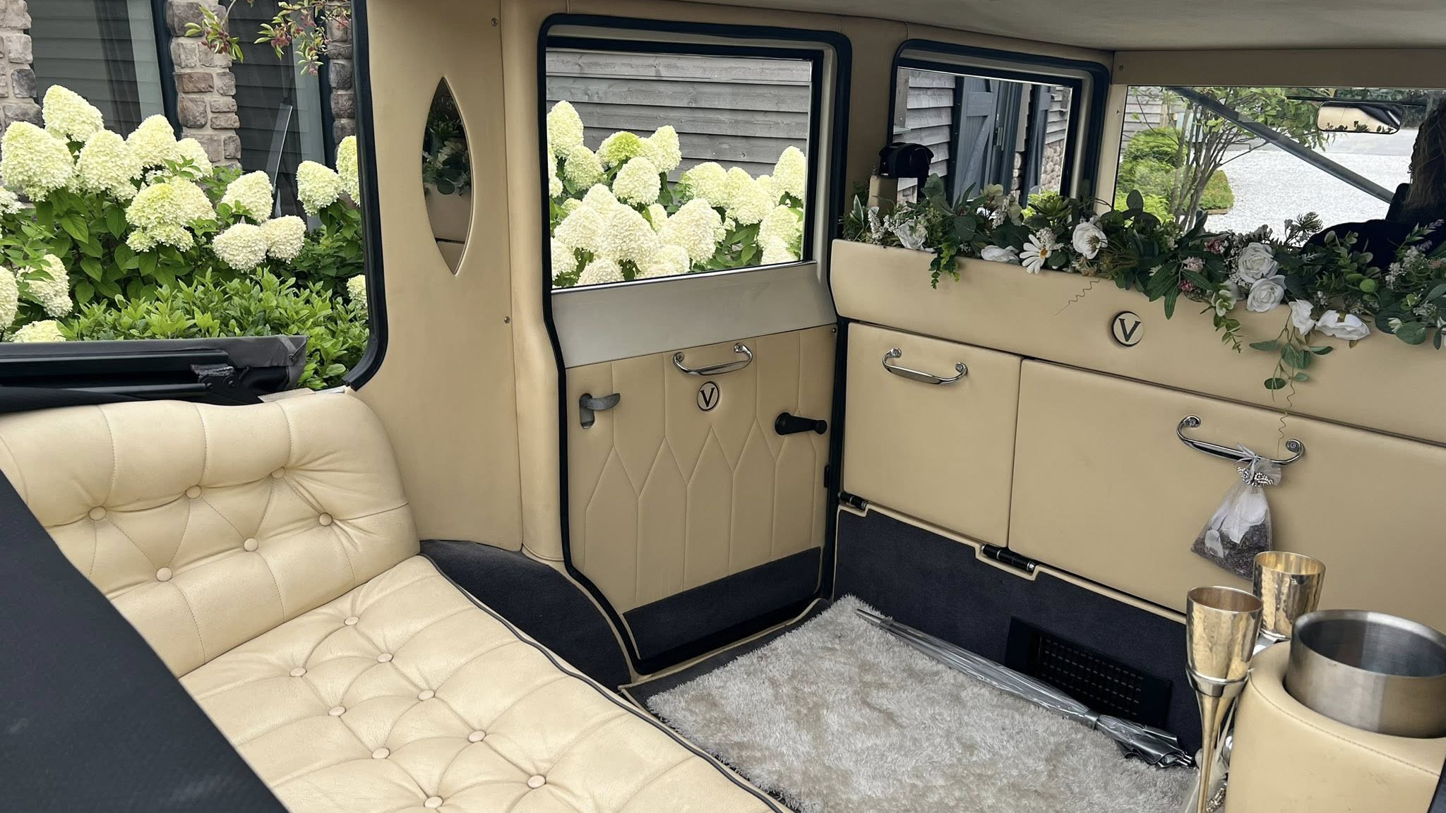 Close-up of the Imperial’s cream leather interior, showing button-back seating, polished wood trim, elegant storage compartments and floral decorations along the windows. The soft natural light highlights the vintage-style craftsmanship and clean detailing.