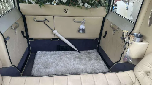 Interior view of the Viscount wedding car showing cream leather seating, button-back upholstery, polished trim and side floral decorations, with windows looking out onto greenery.