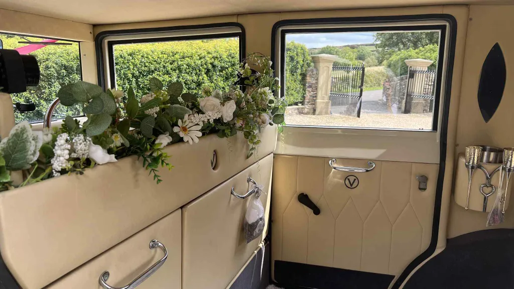 Close-up of cream leather seating inside a vintage wedding car with floral garlands, ivory panels and views of trees outside the window.
