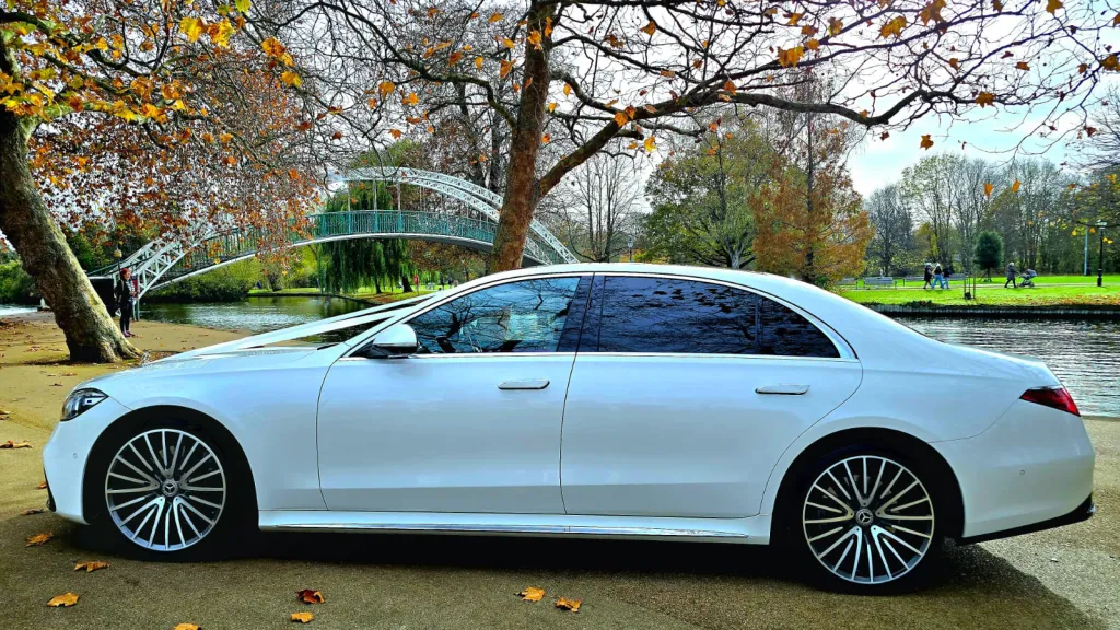 Left side profile of a white Mercedes-Benz S-Class 500 parked on a tree-lined road.