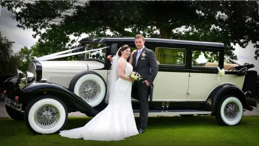 Bride wearing a white dress standing by a vintage style Bramwith wedding car with her groom