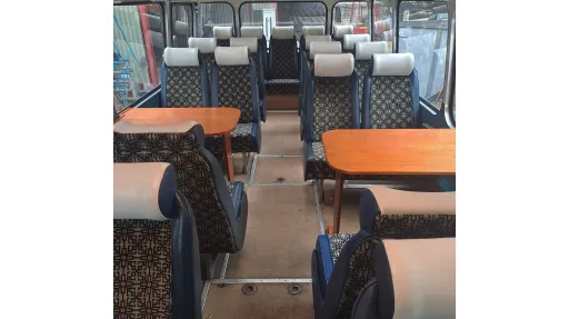 Interior of a vintage single-decker bus with blue and grey patterned seats and wooden flooring, shown from a forward-facing aisle view.
