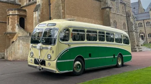 Yellow and green vintage single-decker bus photographed from a front angled view outside a large historic stone building.
