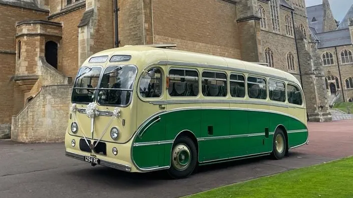 Yellow and green vintage single-decker bus photographed from a front angled view outside a large historic stone building.