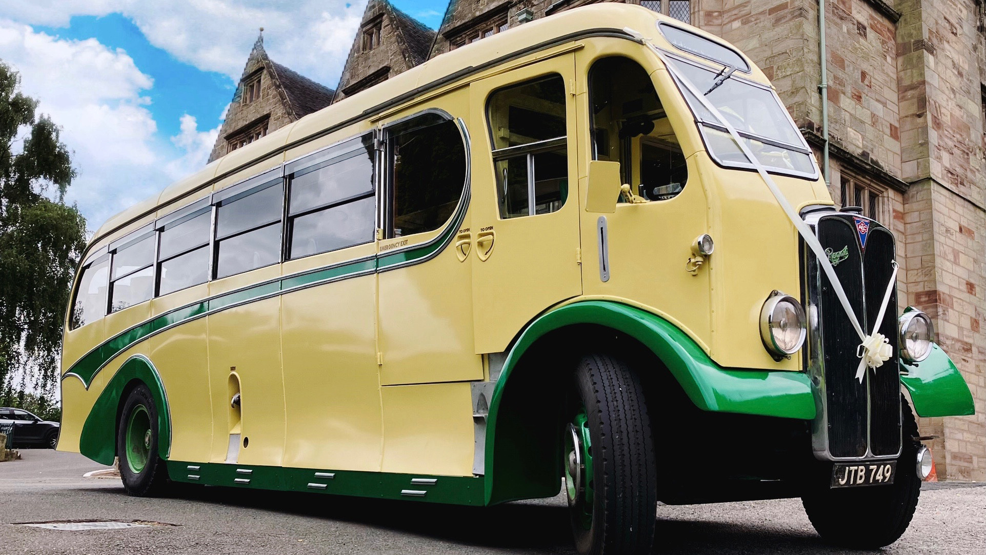 Yellow and green vintage single-decker bus photographed from a low front angled view with stone buildings and cloudy sky behind.
